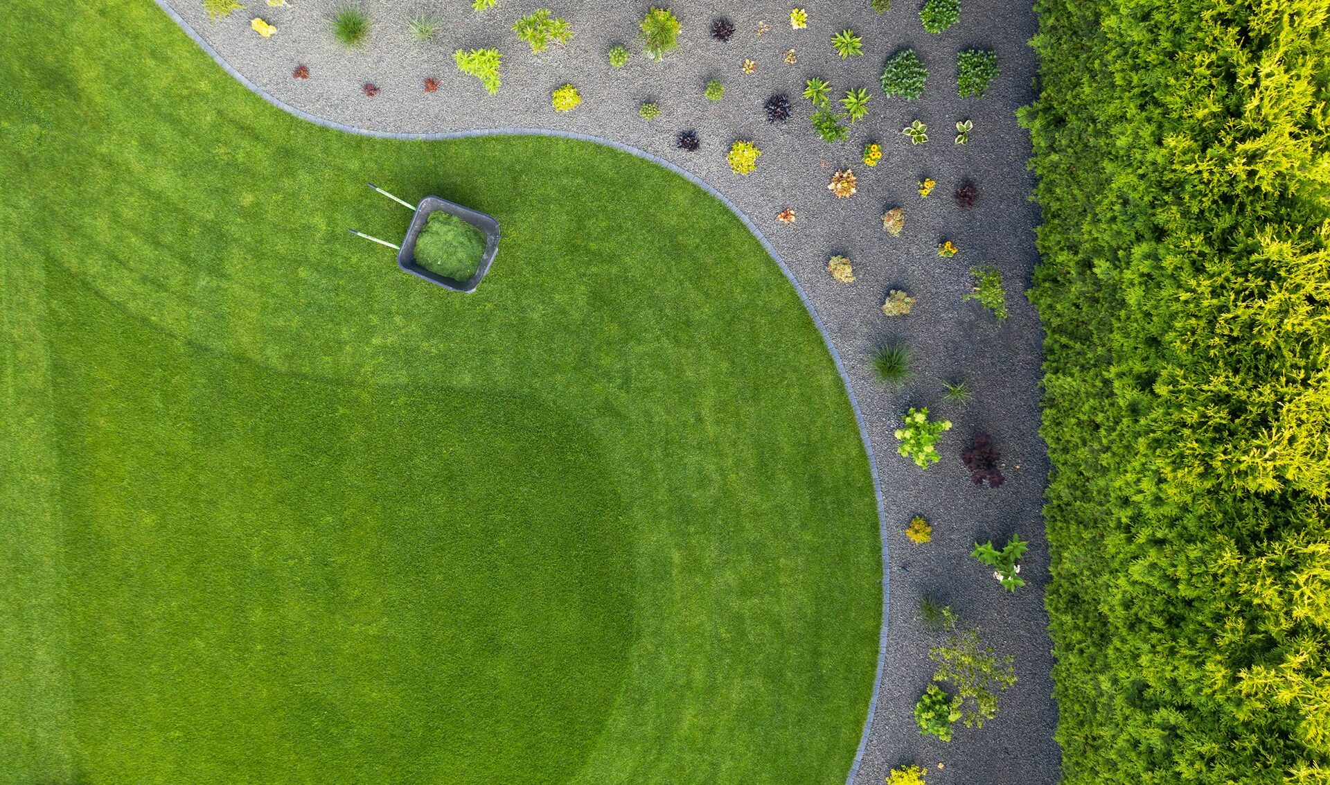 Aerial view of a professionally landscaped residential backyard with a curved lawn and fresh garden beds